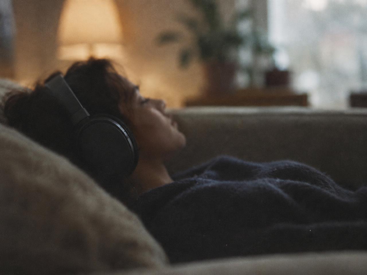 Une personne allongée sur un canapé avec un casque audio, vue de dos