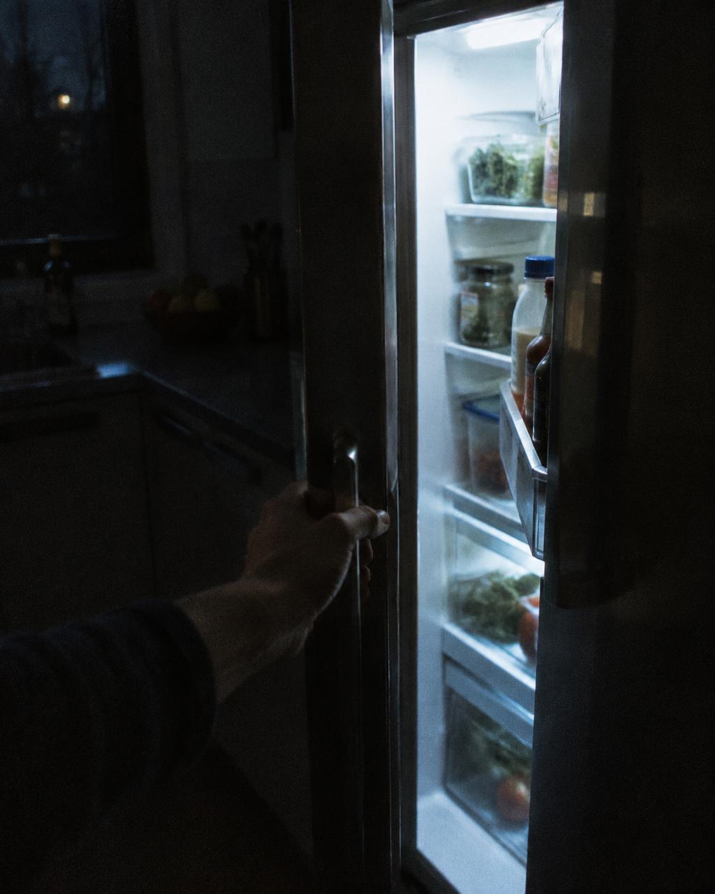 Une cuisine le soir, un placard entrouvert, une main qui hésite